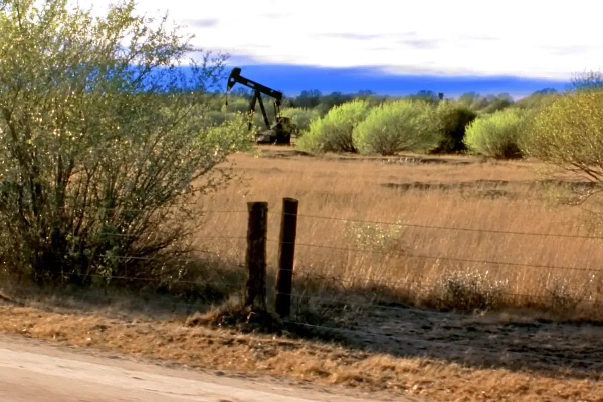 Pumpjack and barbed wire fence on brush country along a caliche road in Atascosa County, Texas