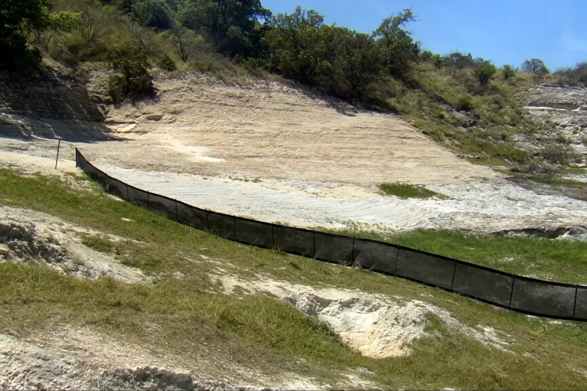 Cut and graded building pad on pale limestone ground behind a silt fence over the Edwards Aquifer recharge zone near San Antonio, Texas