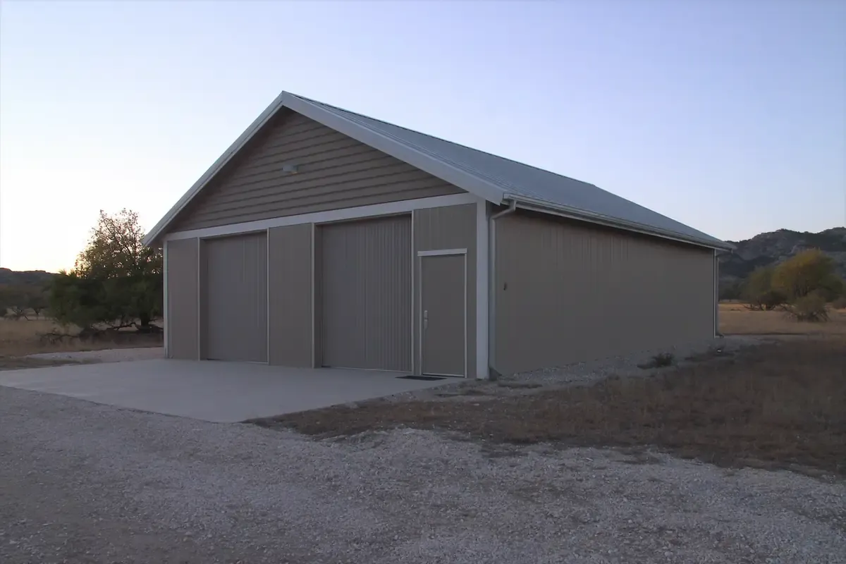 Finished tan metal building with two roll-up doors on a gravel lot in the San Antonio area, Texas