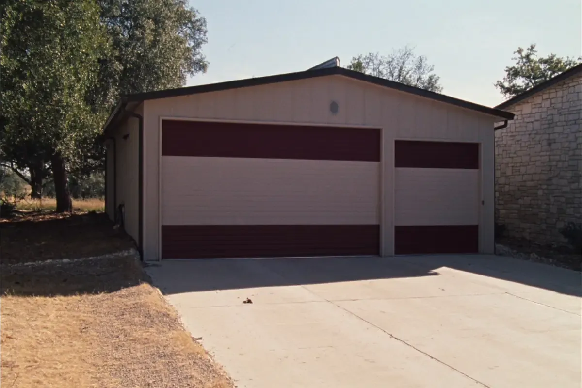 Metal garage building with three dark red roll-up doors on a concrete drive in the San Antonio area, Texas