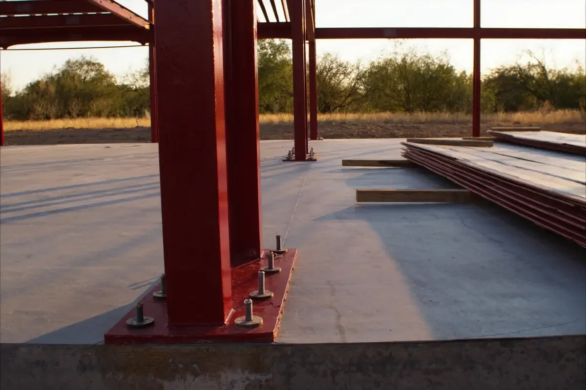 Red primed steel column set on anchor bolts at a slab edge during steel erection in South Texas